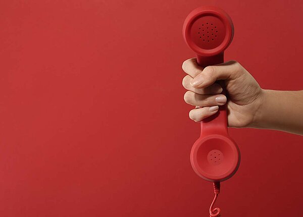 Hand hält rotes Telefon vor rotem Hintergrund hoch.