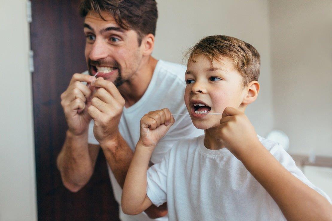 Vater und Sohn benutzen Zahnseide vor dem Spiegel.