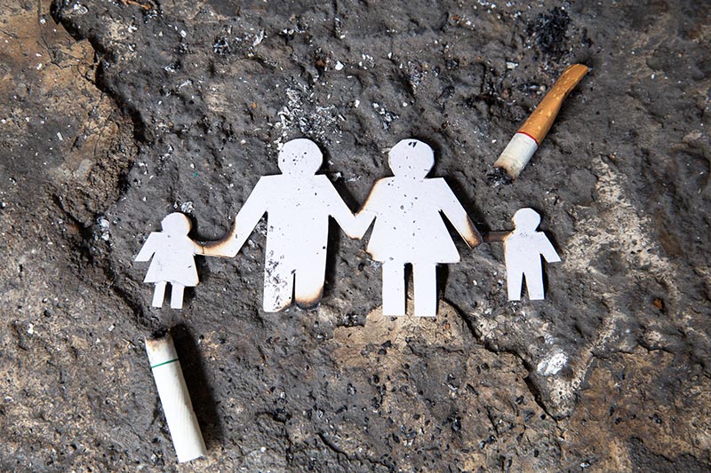 Papierfiguren in Form einer Familie liegen auf einem Stein, darum liegen Zigarettenkippen. 