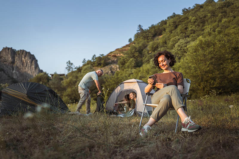 Eine Familie in der Natur: Zwei Kinder im Zelt, ein Mann nimmt etwas aus dem Wanderrucksack und eine Frau sitzt auf einem Campingstuhl.