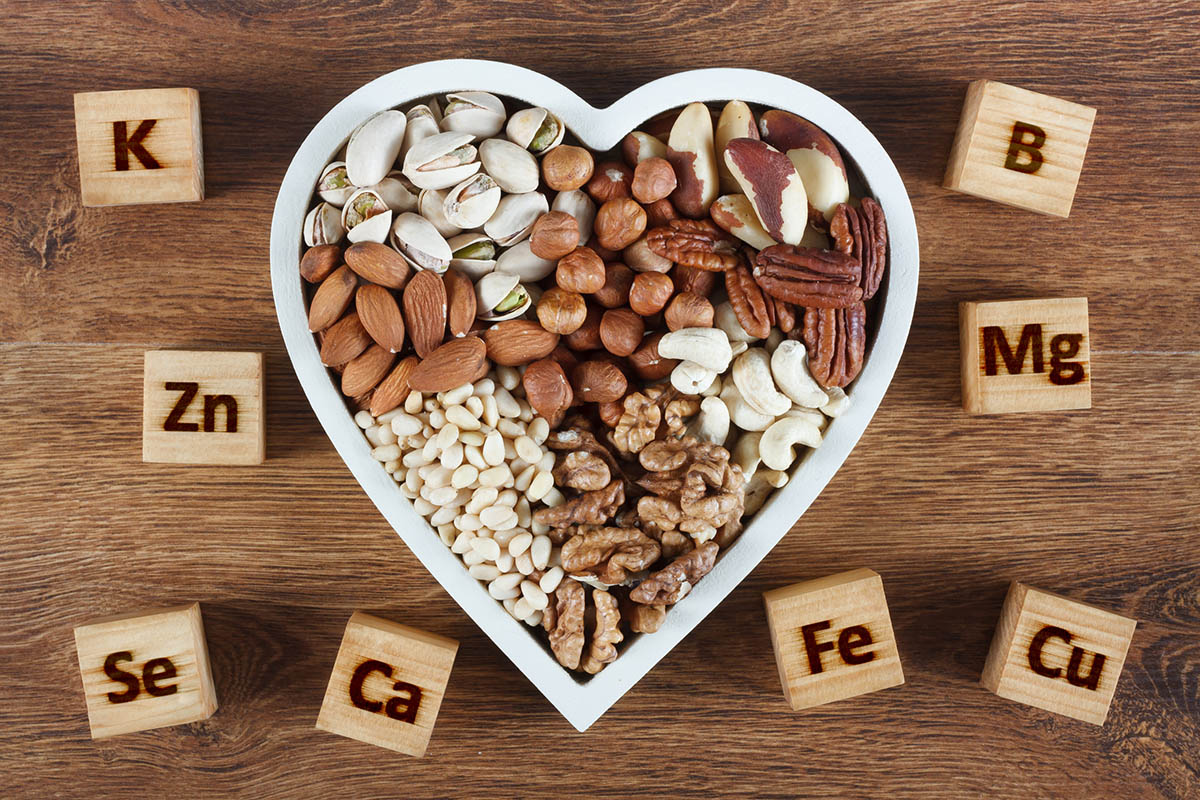 verschiedene Nüsse in einer herzförmigen Schale, darum liegen Holzklötze, die mit verschiedenen Elementen beschriftet sind – zum Beispiel Eisen, Calcium, Selen und Magnesium.