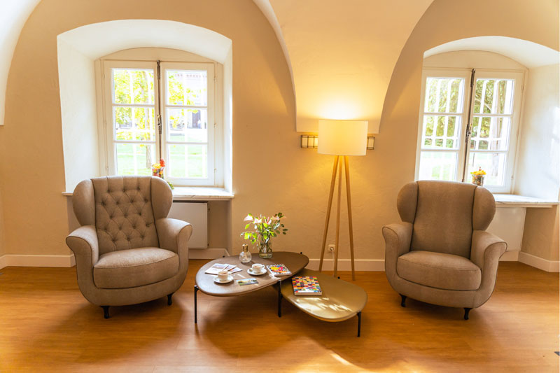 Zwei gemütliche Sessel und niedrige Tische, alles in runden Formen, stehen vor einem Fenstergewölbe.