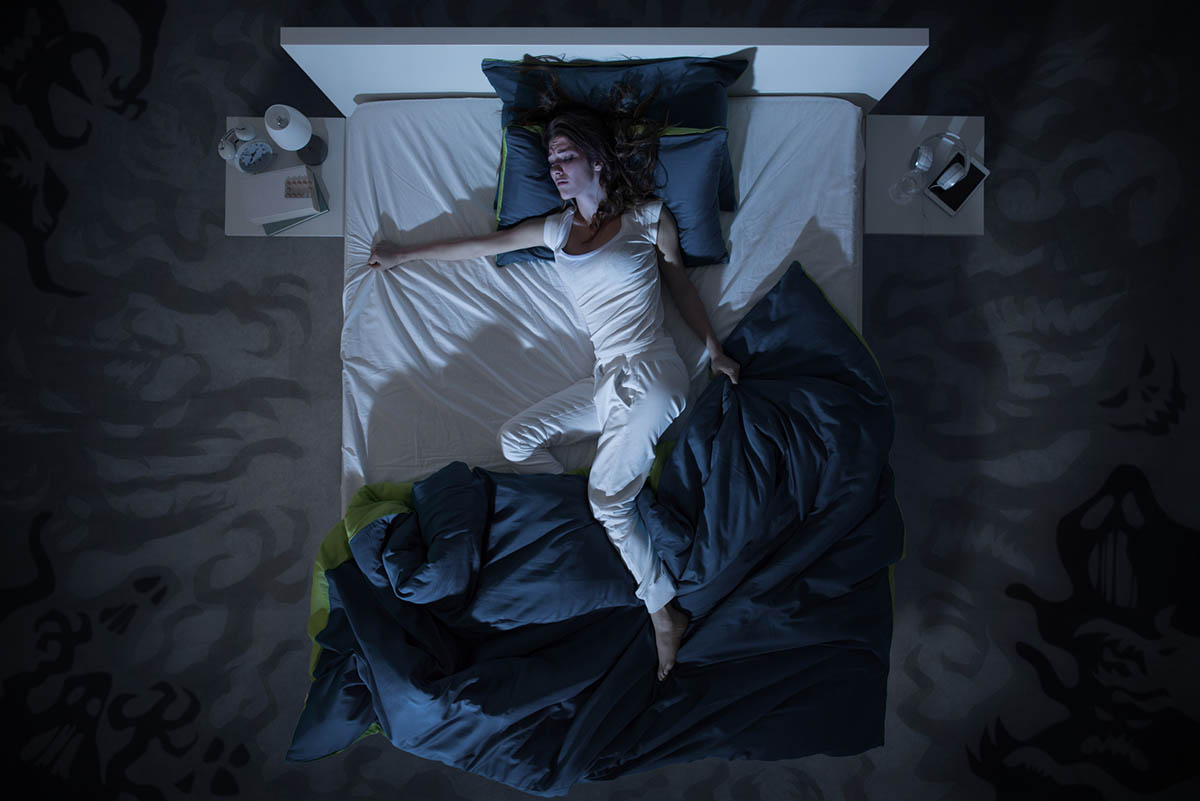 Eine Frau liegt im Bett, hat sich aus der Decke gewühlt und verzieht das Gesicht.