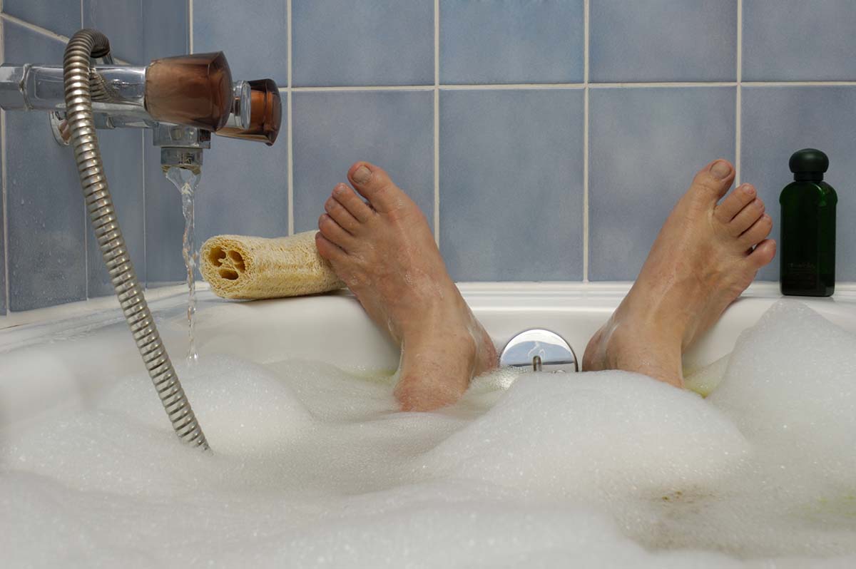 Neurodermitis pflegen Aus Sicht einer badenden Person: Ein Haufen Schaum, der Wasserhahn der Badewanne und eine altmodisch gekachelte Wand.