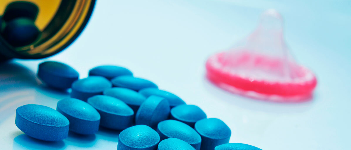 Blaue Tabletten liegen vor einer Tablettendose und in der Ecke liegt ein Kondom