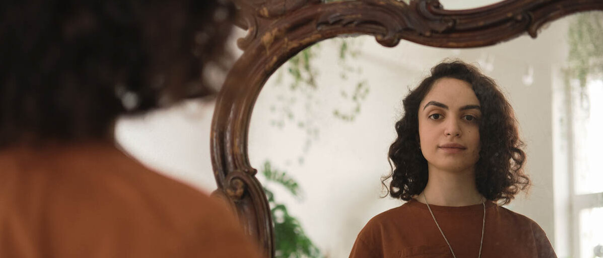 Eine junge Frau blickt in den Spiegel.