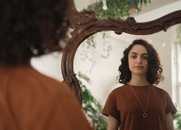 Eine junge Frau blickt in den Spiegel.