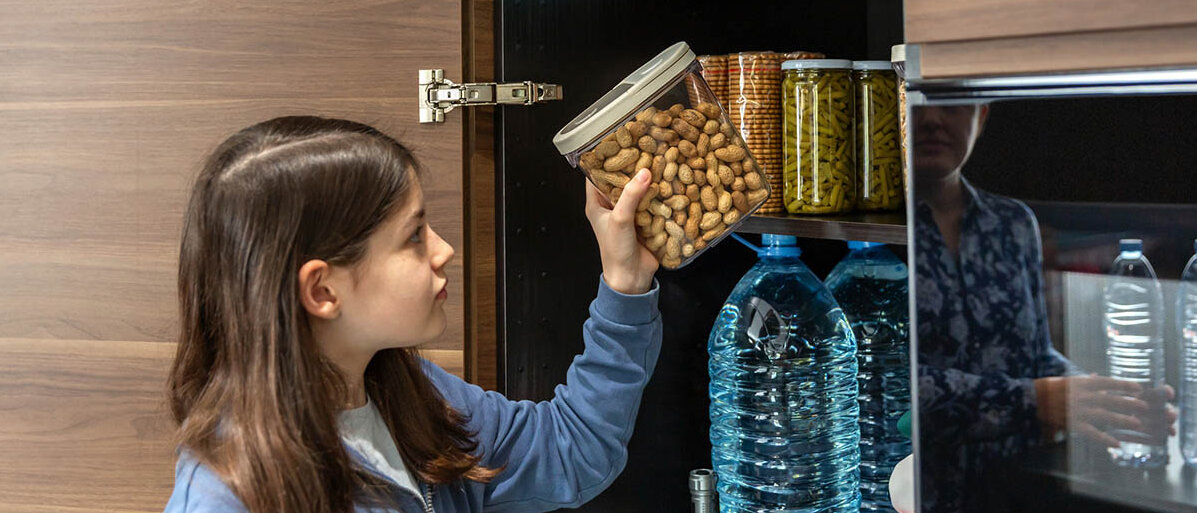 Ein Mädchen stellt ein Vorratsglas mit Erdnüssen in den Schrank.
