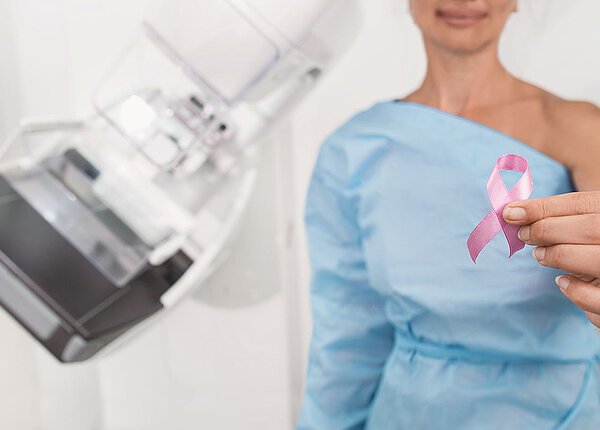 Frau vor Mammograph zeigt rosa Brustkrebsschleife 