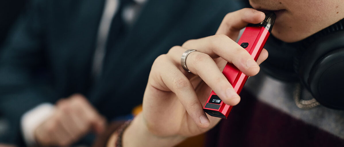 Gesicht eines Jugendlichen, der eine E-Zigarette raucht.