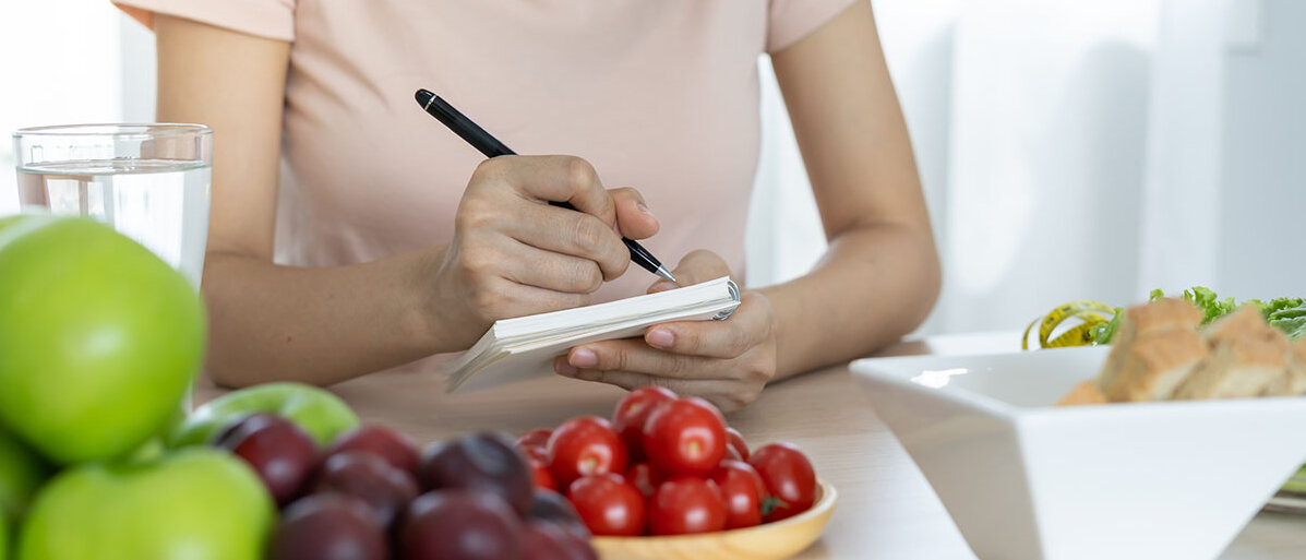 Gewohnheiten ändern Frau mit Notizblock an einem Tisch mit gesundem Obst und Gemüse