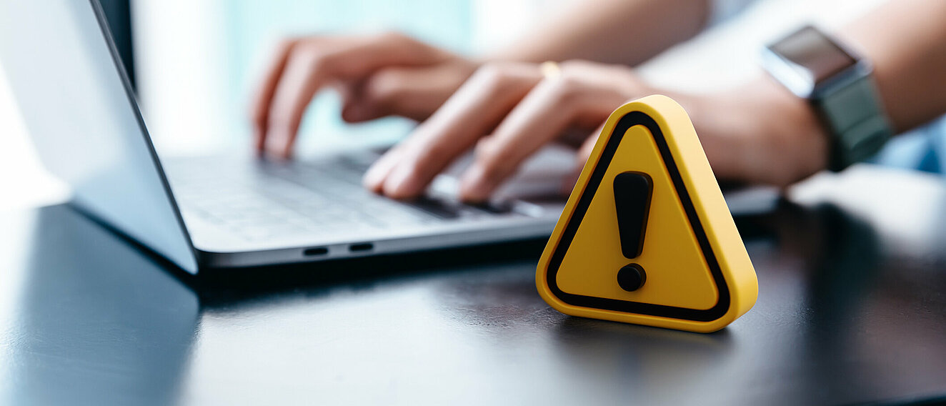 Neue Diclofenac Nebenwirkung Ein Mann sitzt an einem Laptop, davor ein kleines, gelbes Achtung-Schild.