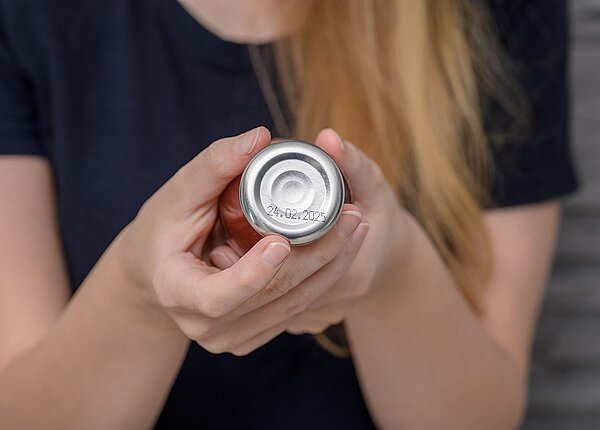 Frau prüft Flasche mit Tomatensoße, auf deren Deckel man ein Mindesthaltbarkeitsdatum erkennt.