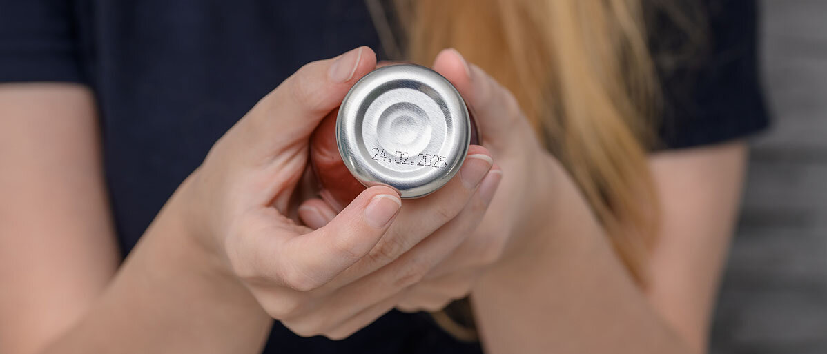 Frau prüft Flasche mit Tomatensoße, auf deren Deckel man ein Mindesthaltbarkeitsdatum erkennt.