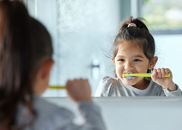 Karies bei Kindern vermeiden : Kleines Mädchen putzt sich vorm Spiegel die Zähne