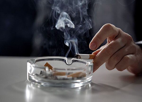 Nahaufnahme: Mann hält brennende Zigarette über Aschenbecher 