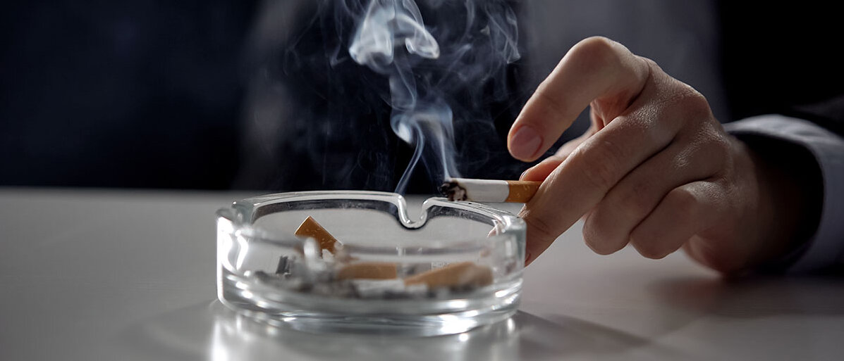 Nahaufnahme: Mann hält brennende Zigarette über Aschenbecher 