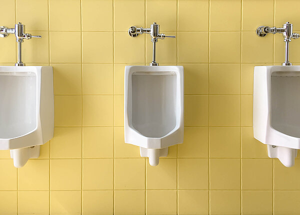 Drei weiße Prozellanurinale an einer gelb gefliesten Wand