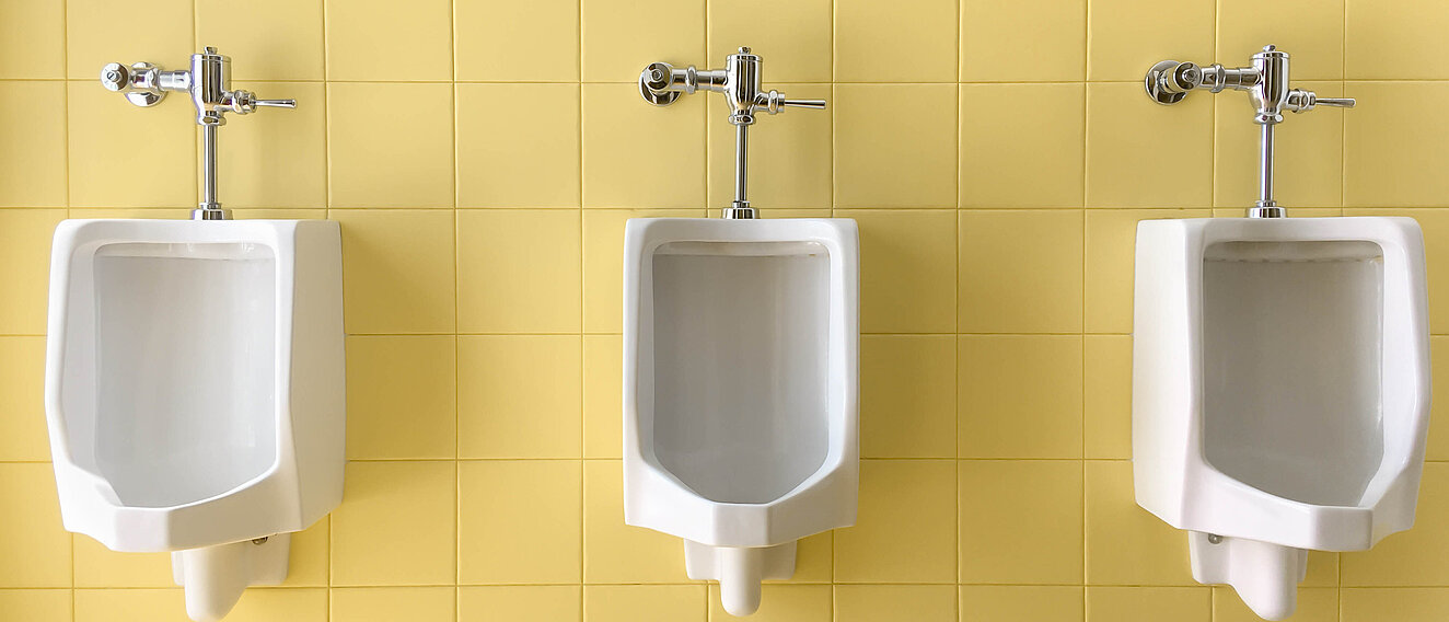 Drei weiße Prozellanurinale an einer gelb gefliesten Wand