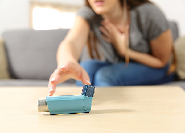 Eine Frau greift sich ans Dekolletee. Sie greift nach ihrem blauen Asthma-Spray.