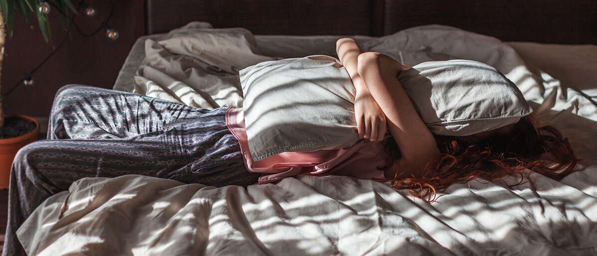 Dauerkrisen und Zukunftsängste Traurige junge Frau, die mit Kissen auf dem Gesicht im Bett liegt