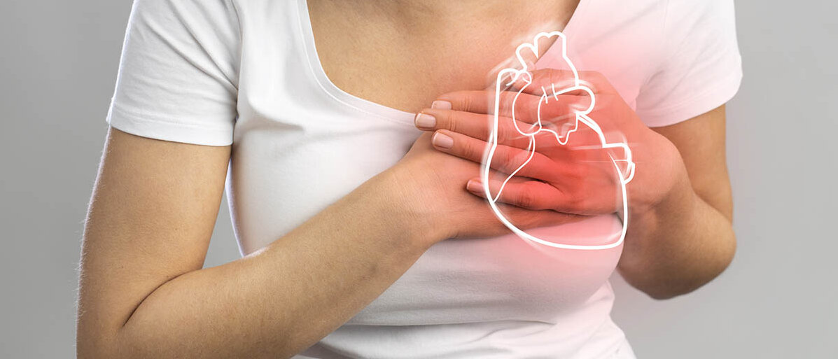 Koronarspasmen: Der Herzinfarkt bei der Frau hat andere Symptome Eine Frau fasst sich an die Brust. Dort illustriert ist ein anatomisches Herz, das rot leuchtet.