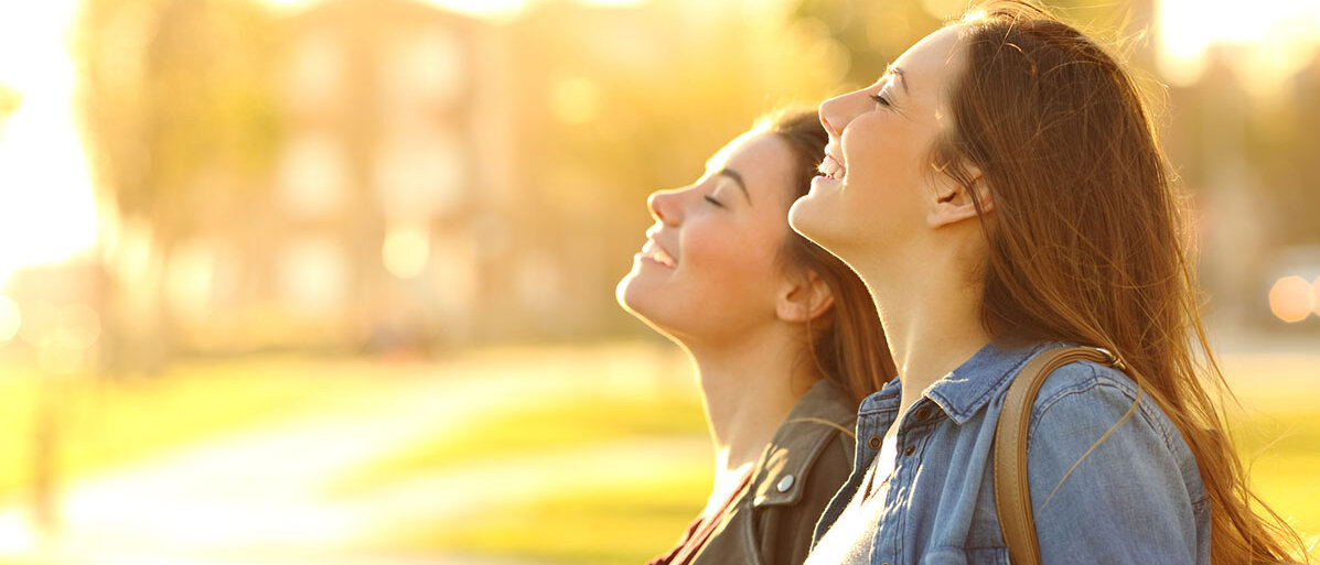 Zwei Frauen stehen nebeneinander, schauen nach oben und genießen die Sonne