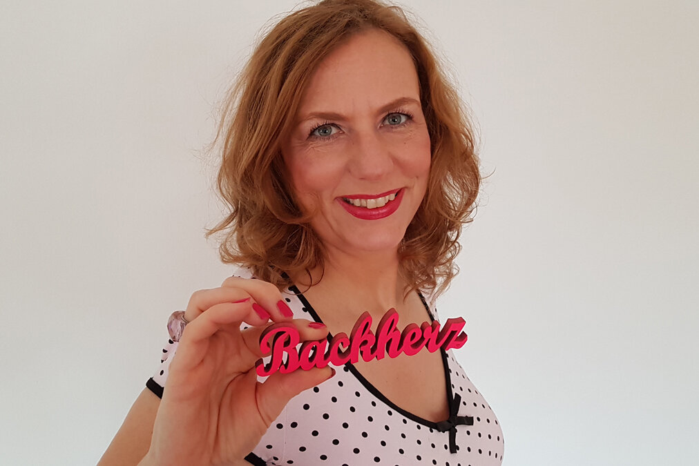 Rezeptautorin Kirsten Metternich von Wolff lächelt und hält einen Holz-Schriftzug in die Kamera: "Backherz".
