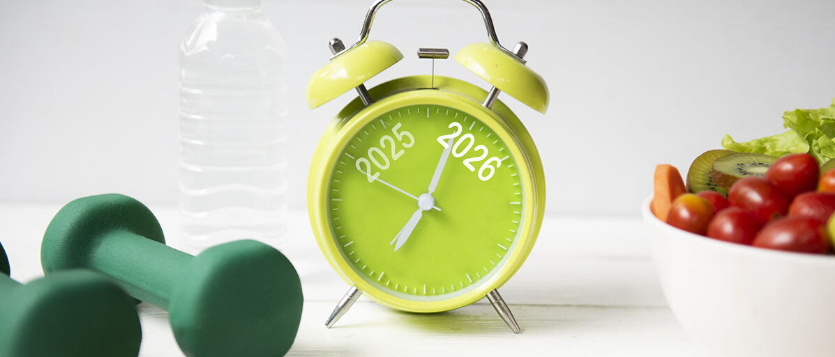 Gemüse, Obst, Hanteln und Maßband neben einer Wasserflasche und einem Wecker auf dem 2025 und 2026 steht 
