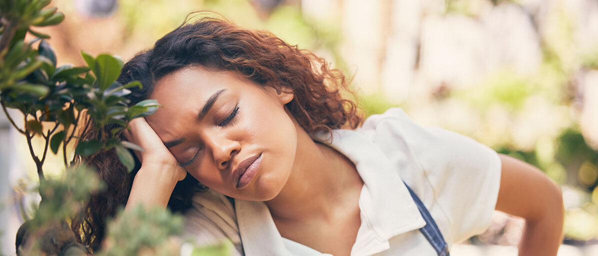 Afrodeutsche Frau nickt bei der Gartenarbeit im Stehen weg