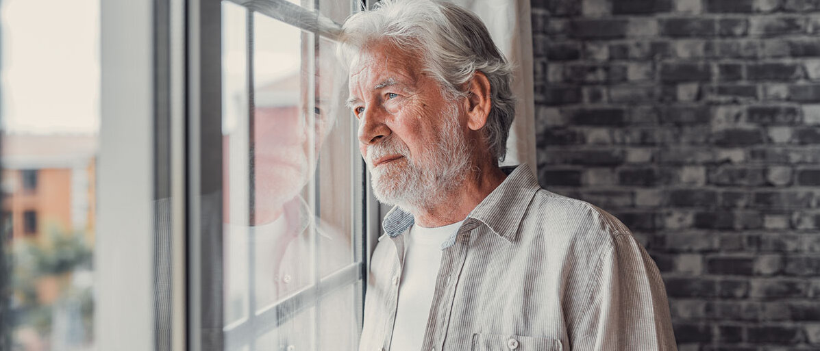 Erste Anzeichen einer Demenz ernst nehmen Nachdenklicher älterer Mann mit, der aus dem Fenster schaut