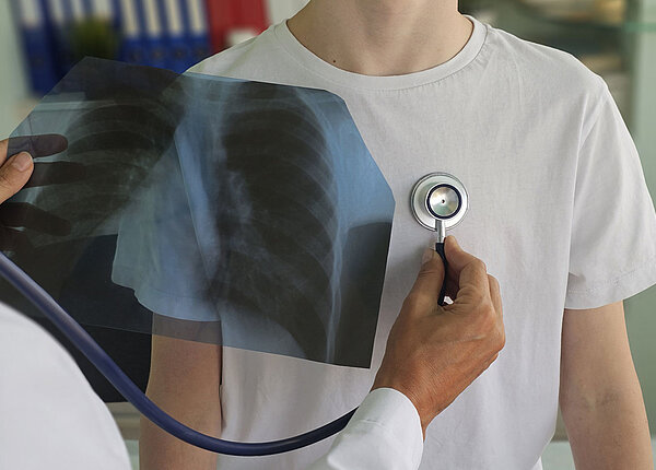 Arzt mit Röntgenbild einer Lunge in der Hand untersucht Brustkorb eines Jungen mit Stethoskop 