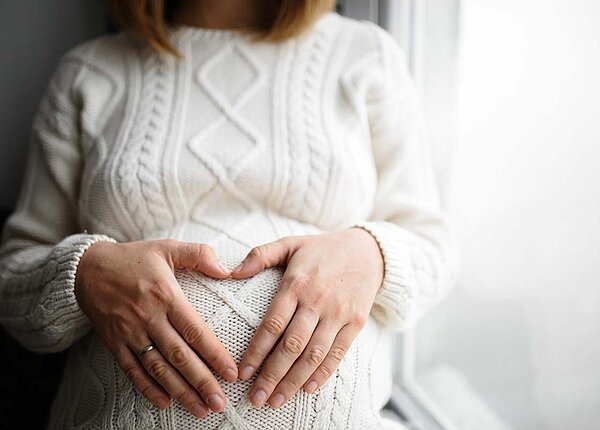 Schwangere Frau mit Händen auf dem Bauch.