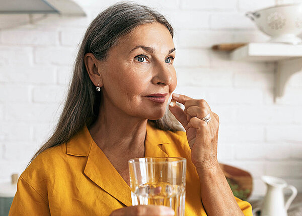 Eine Frau mit langen, grauen Haaren nimmt eine Weichkapsel ein.