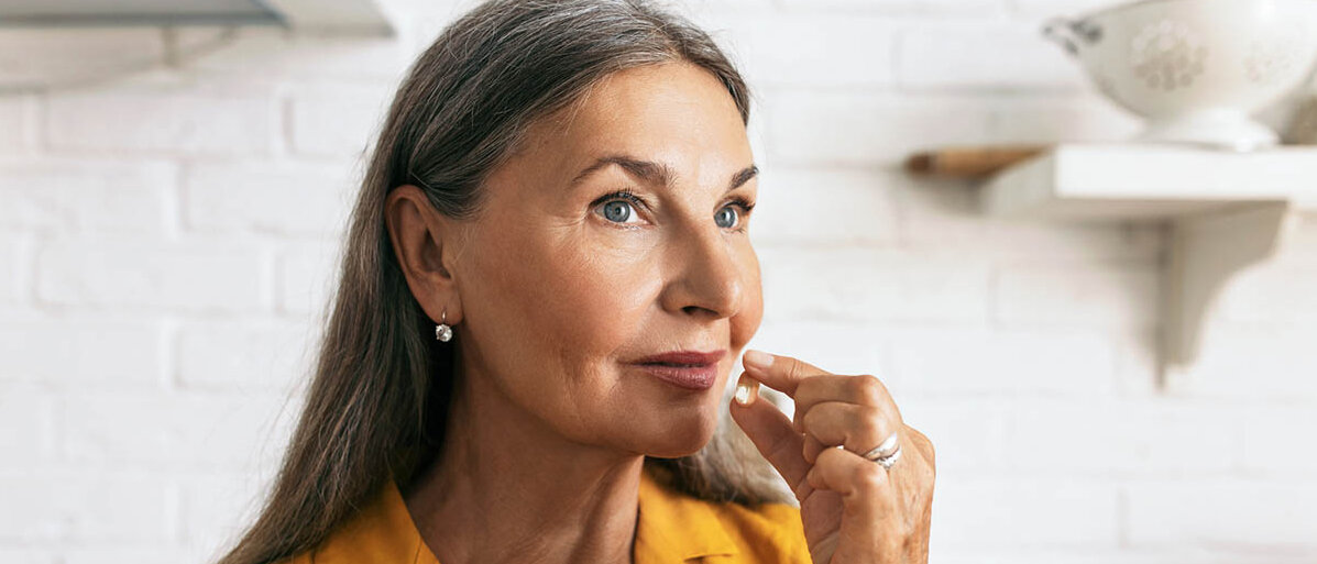 Eine Frau mit langen, grauen Haaren nimmt eine Weichkapsel ein.