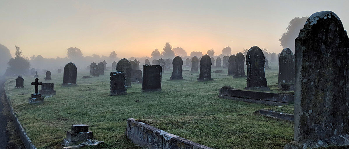 Ein Friedhof mit alten, verwitterten und moosbewachsenen Grabstein im Nebel der Morgendämmerung