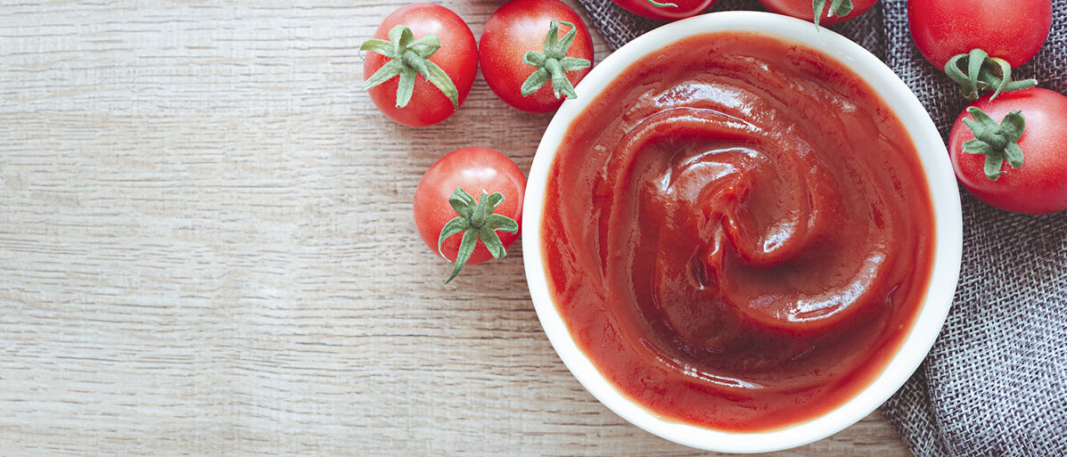 Ketchup in einer Schuessel und drum herum Tomaten