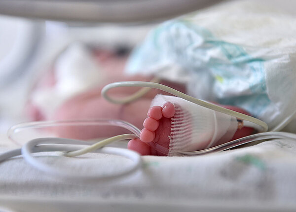 Der Fuß eines neugeborenen Babys im Klinikbett: Ein Schlauch ist mit Verbandmull befestigt.
