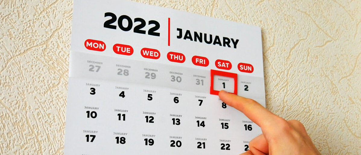 Auf einem Wandkalender ist der 1. Januar 2022 mit einem roten Rahmen markiert. Ein Finger hält den roten Rahmen und wird ihn wohl gleich verschieben.