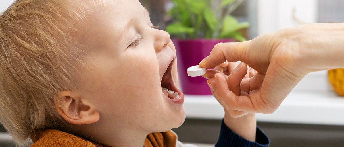Ein Kleinkind bekommt eine große Tablette in den Mund gelegt.