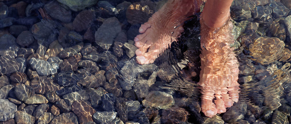 Barfuß auf runden Kieseln im flachen Wasser