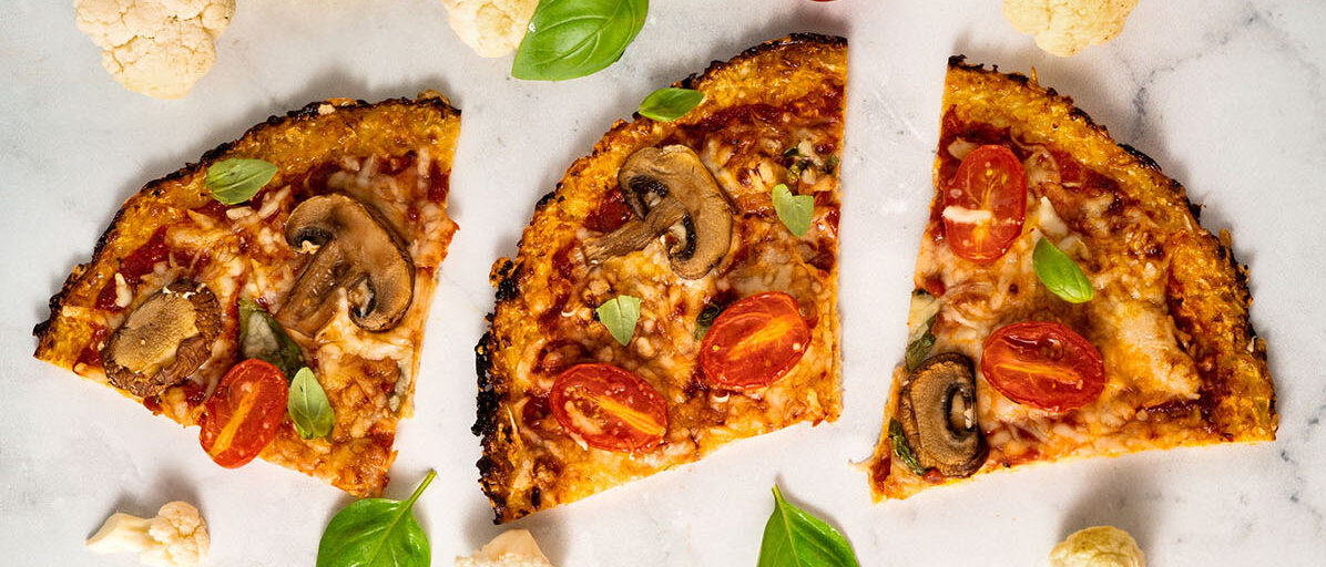 Drei Pizzastücke belegt mit Pilzen, Cherry-Tomaten, Tomatensoße und Käse. Der Pizzaboden ist aus Blumenkohl. 