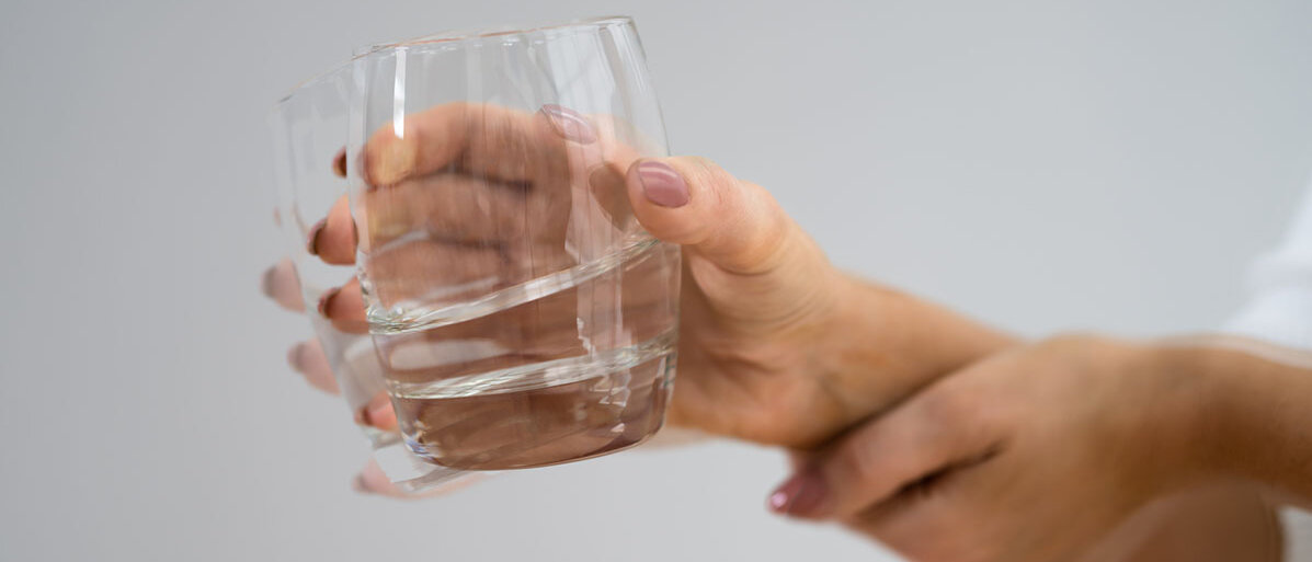 Frau hält ein volles Wasserglas in der Hand und die andere Hand unterstützt