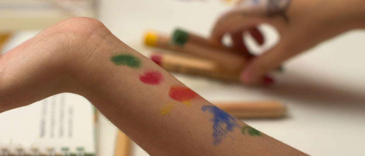 Ein Kind malt sich mit Stiften verschiedenfarbige Punkte auf den Arm.