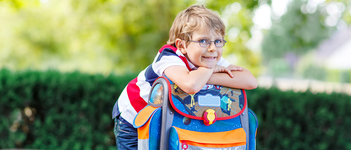 Ein Kind mit Brille stützt sich auf einen Schulrucksack ab