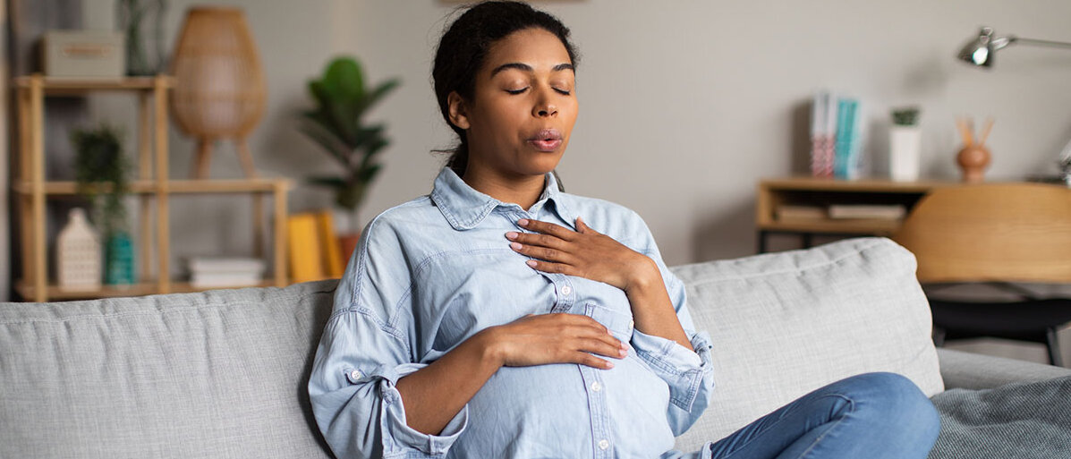 Eine schwangere afroamerikanische Frau macht Atemübungen auf dem Sofa 