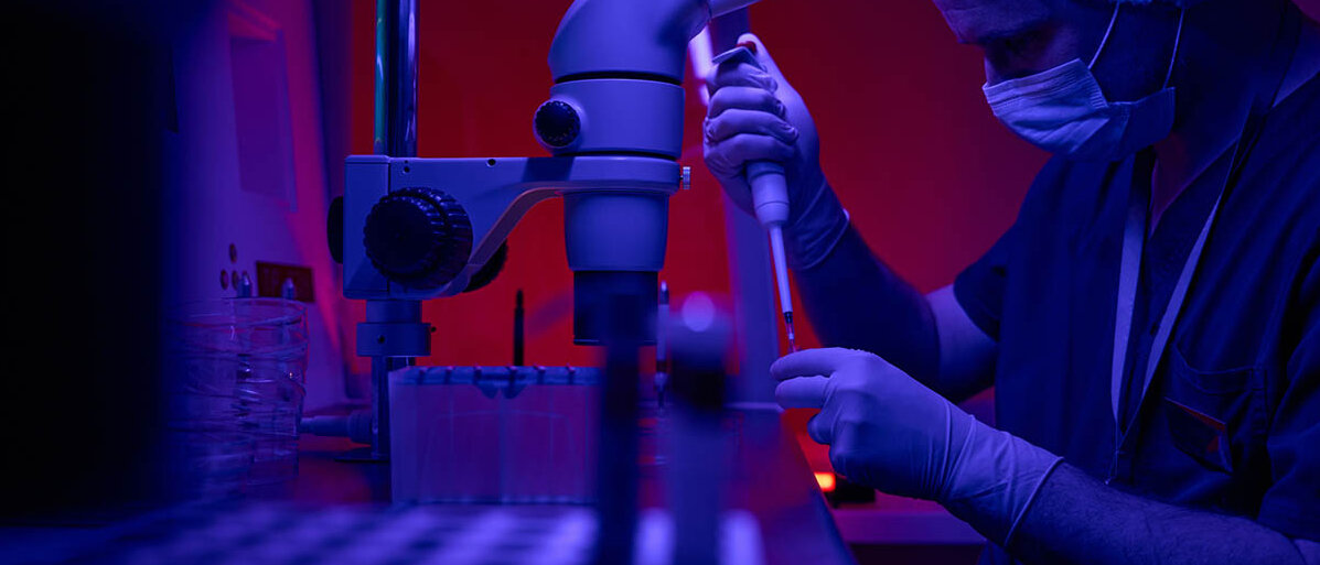 Cannabis und Kinderwunsch Forscher mit Kittel, Handschuhen und Maske pipettiert vor Mikroskop