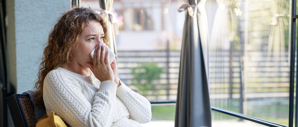 Frau putz sich die Nase vor Fenstern mit Schutzgitter