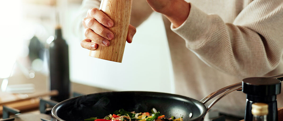 Mann mit hölzerner Pfeffermühle würzt Essen.