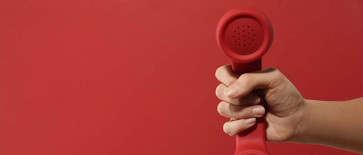 Hand hält rotes Telefon vor rotem Hintergrund hoch.